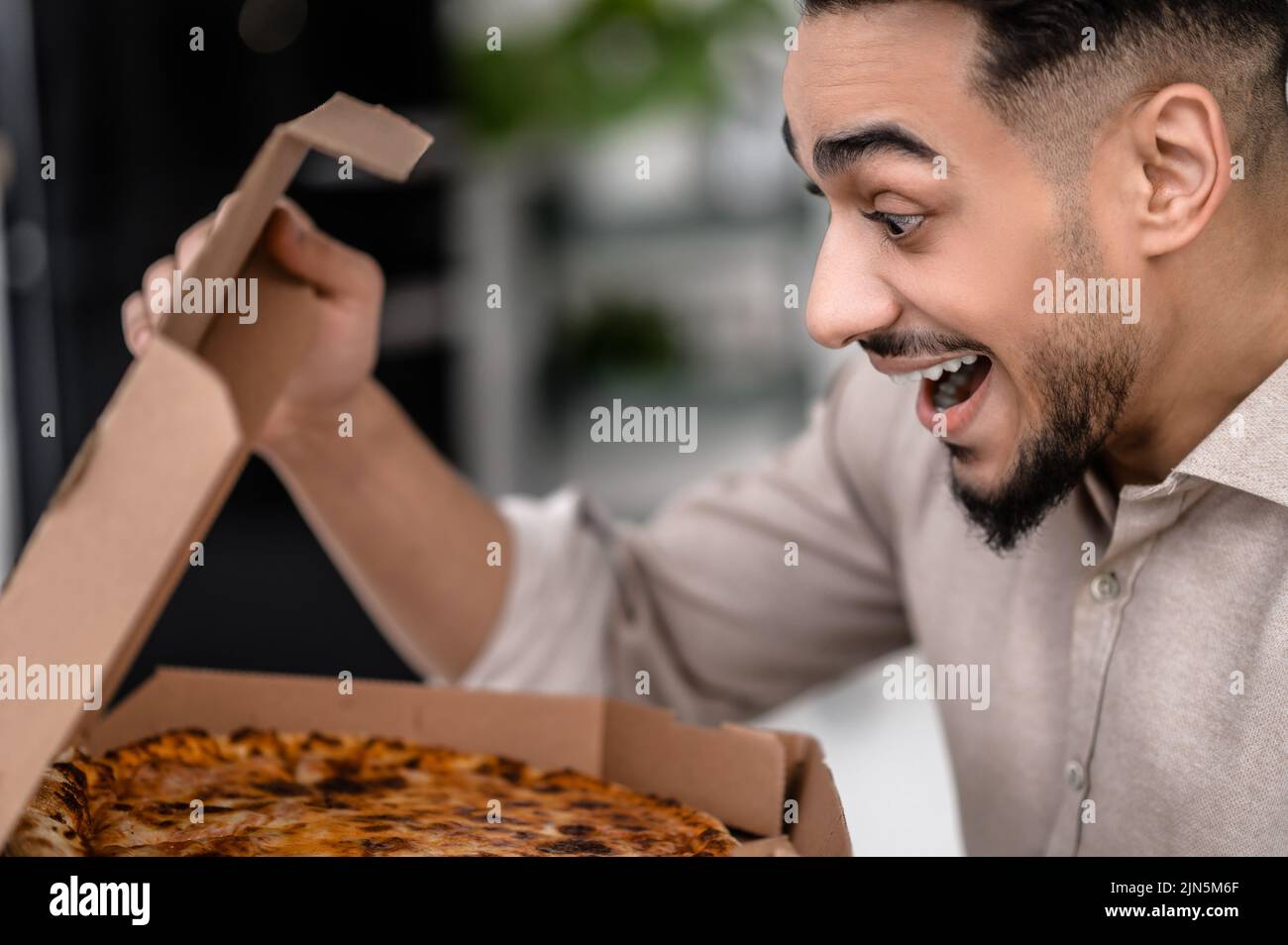 Mann seitlich zur Kamera blickt begeistert auf Pizza Stockfoto
