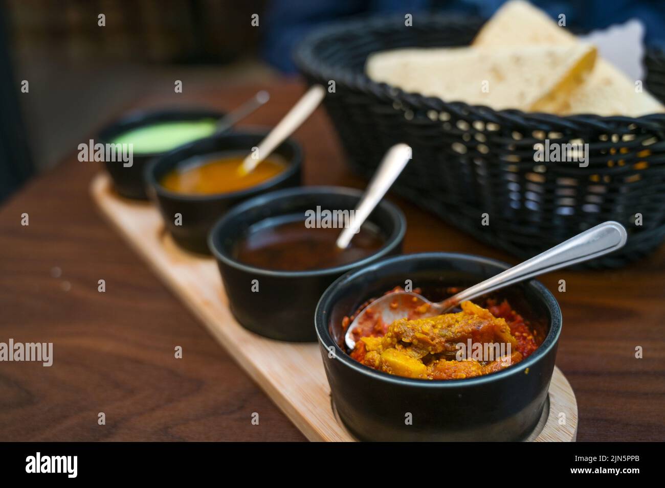 Indische Dip, Relish, Chutney und Sauce in kleinen schwarzen Schalen mit knusprigem Papadam-Brot auf einem dunklen Holztisch serviert, Kopierraum, ausgewählter Fokus, sehr n Stockfoto
