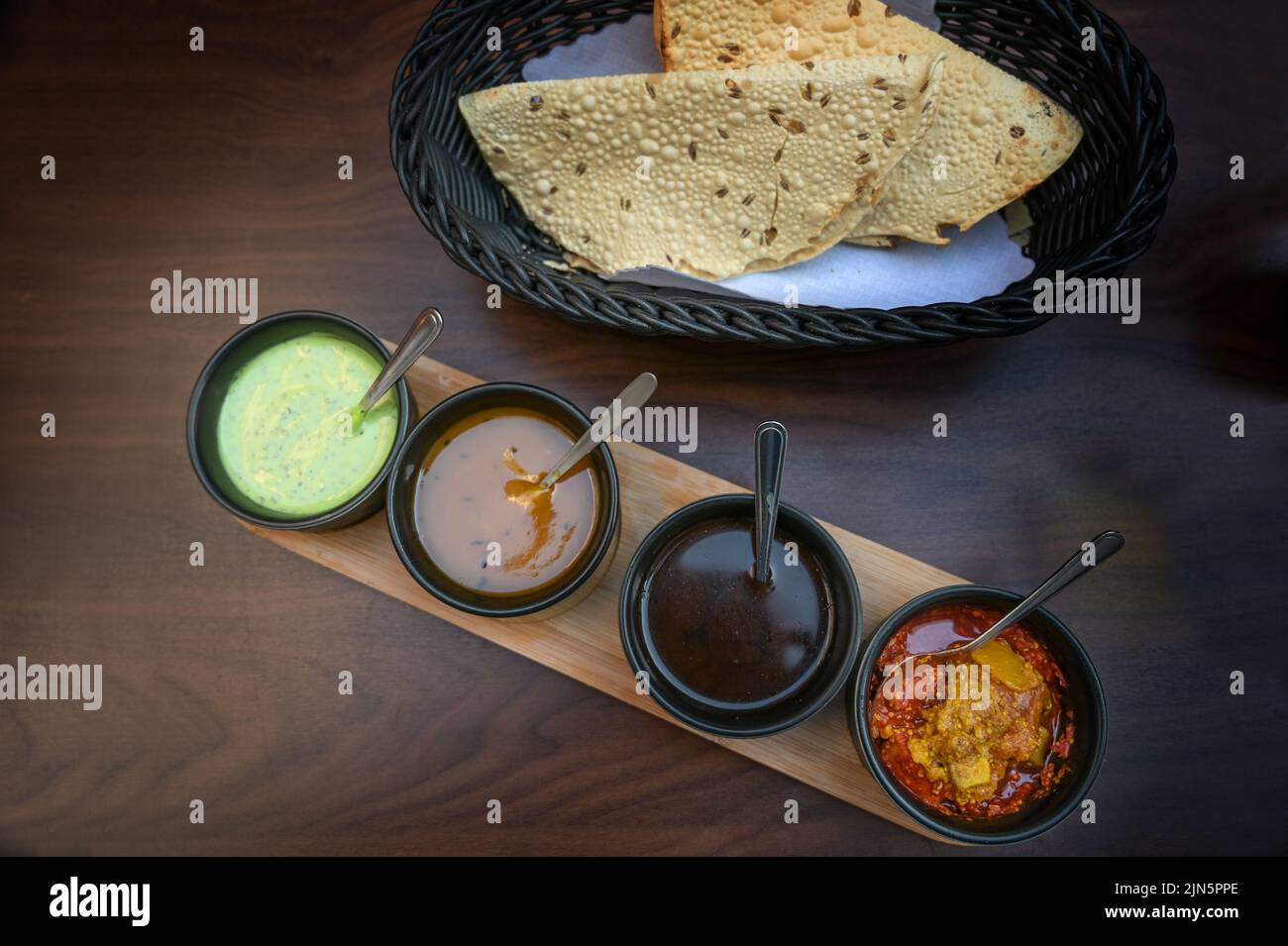 Indische Dip, Relish, Chutney und Sauce in kleinen schwarzen Schalen mit knusprigem Papadam-Brot auf einem dunklen Holztisch serviert, Kopierer Platz, Blick von einem Stockfoto