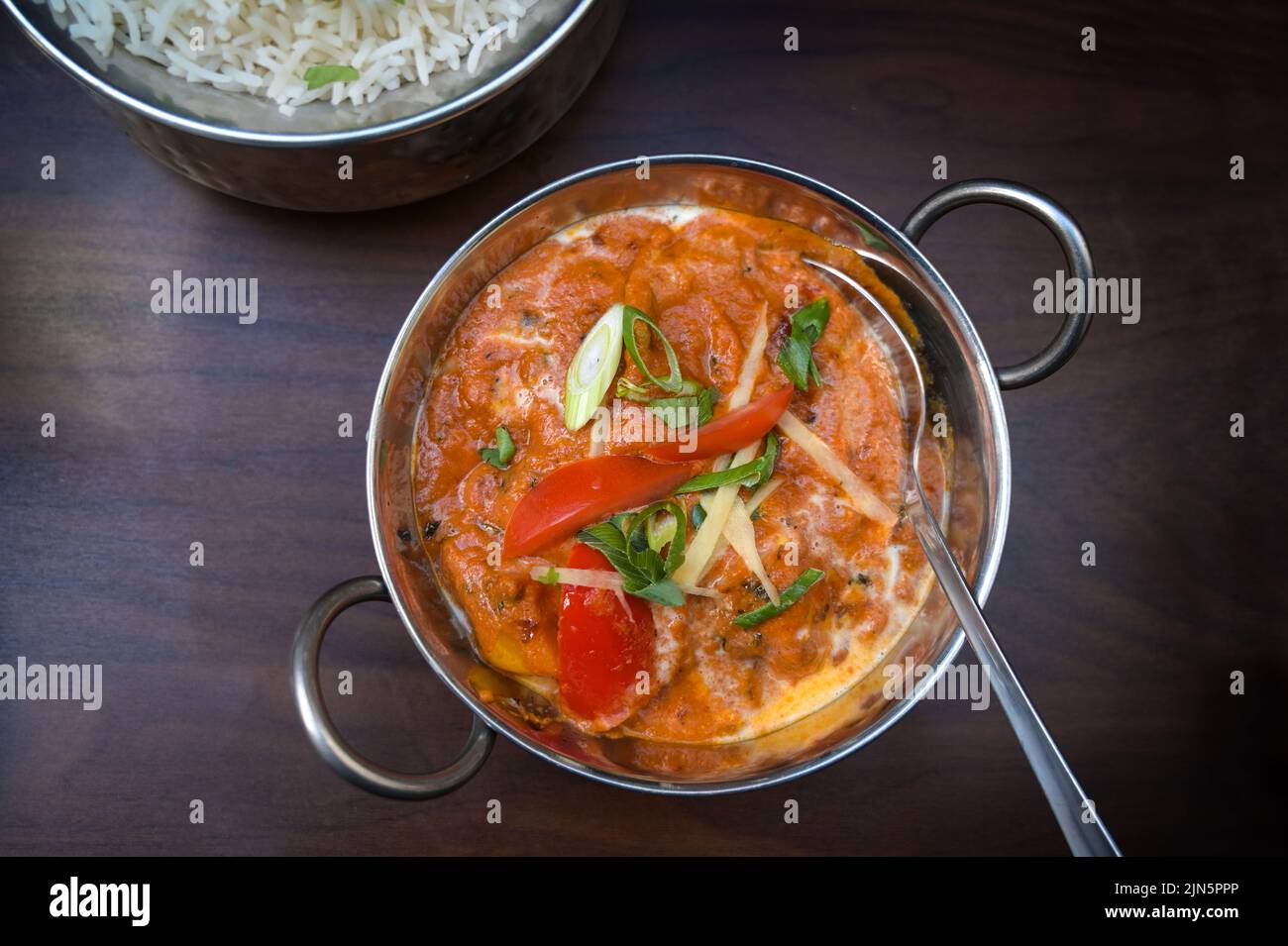 Indisches vegetarisches Gericht mit Tomaten und Frühlingszwiebeln in einer Edelstahlschüssel serviert mit Reis auf einem dunkelbraunen Holztisch, Kopierplatz, hoch Stockfoto