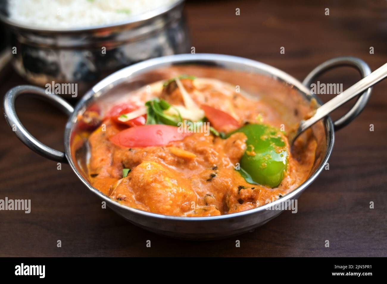 Indisches Hühnchen-Pudergericht mit Gemüse in einer Stahlschüssel serviert mit Reis auf einem dunkelbraunen Holztisch, Kopierraum, ausgewählter Fokus, enge Tiefe von f Stockfoto