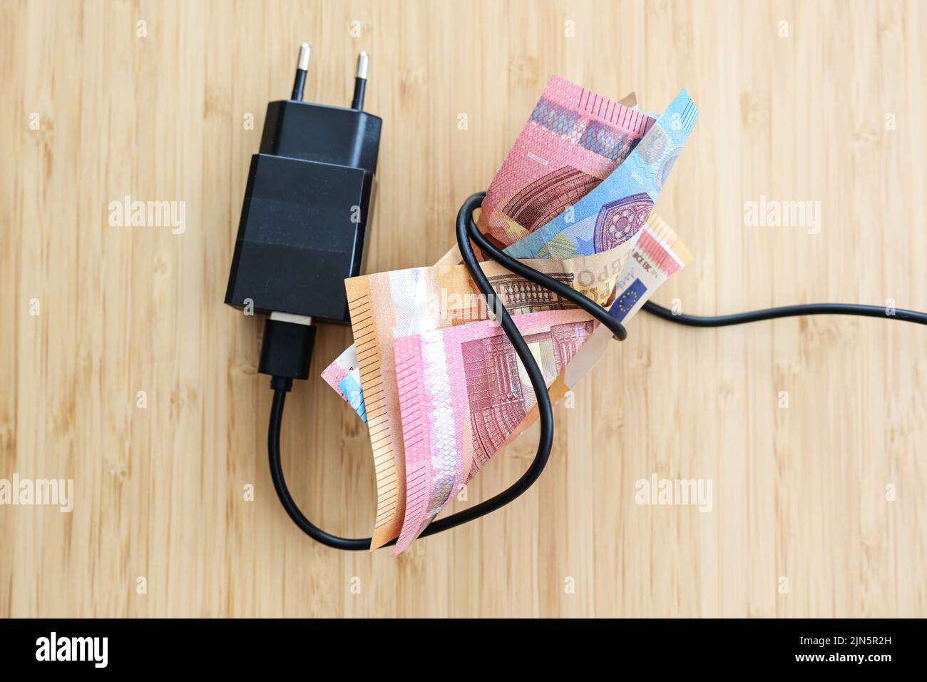 Elektrokabel mit Stecker, der ein Paket von Euro-Banknoten auf einem Holztisch umwickelt, Konzept für Inflation und steigende Energiepreise, Kopierraum, hoch Stockfoto