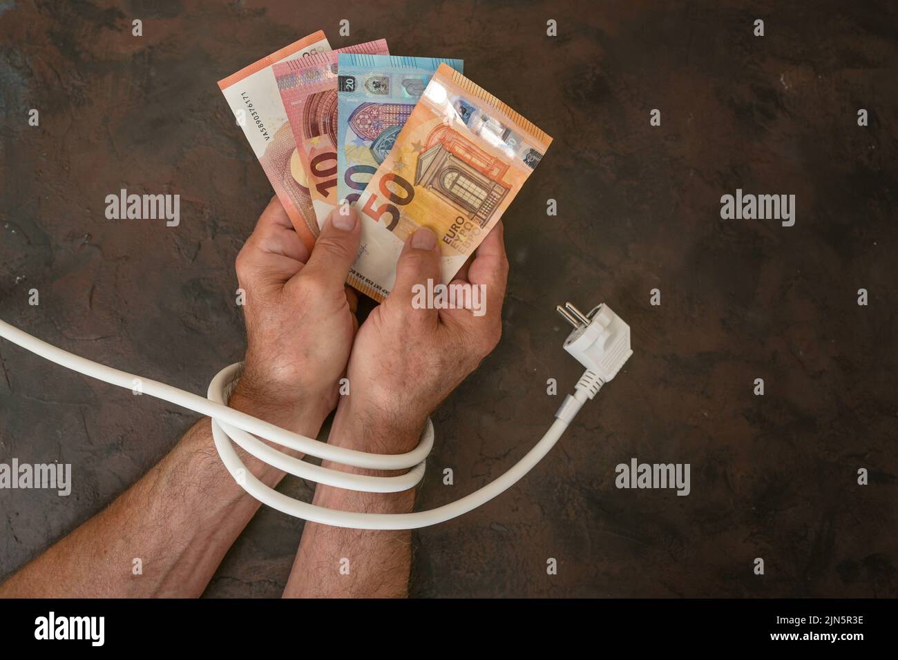 Hände eines Mannes mit Euro-Banknoten und sind mit einem Stromkabel gebunden, Konzept für steigende Stromkosten und Energieeinsparung, dunkle Backgrou Stockfoto