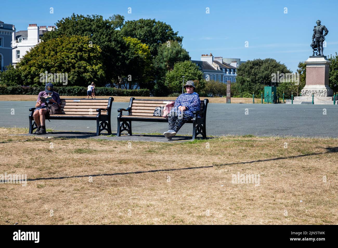 Menschen, die an einem heißen, sonnigen Tag auf einer Bank in Plymouth sitzen Stockfoto