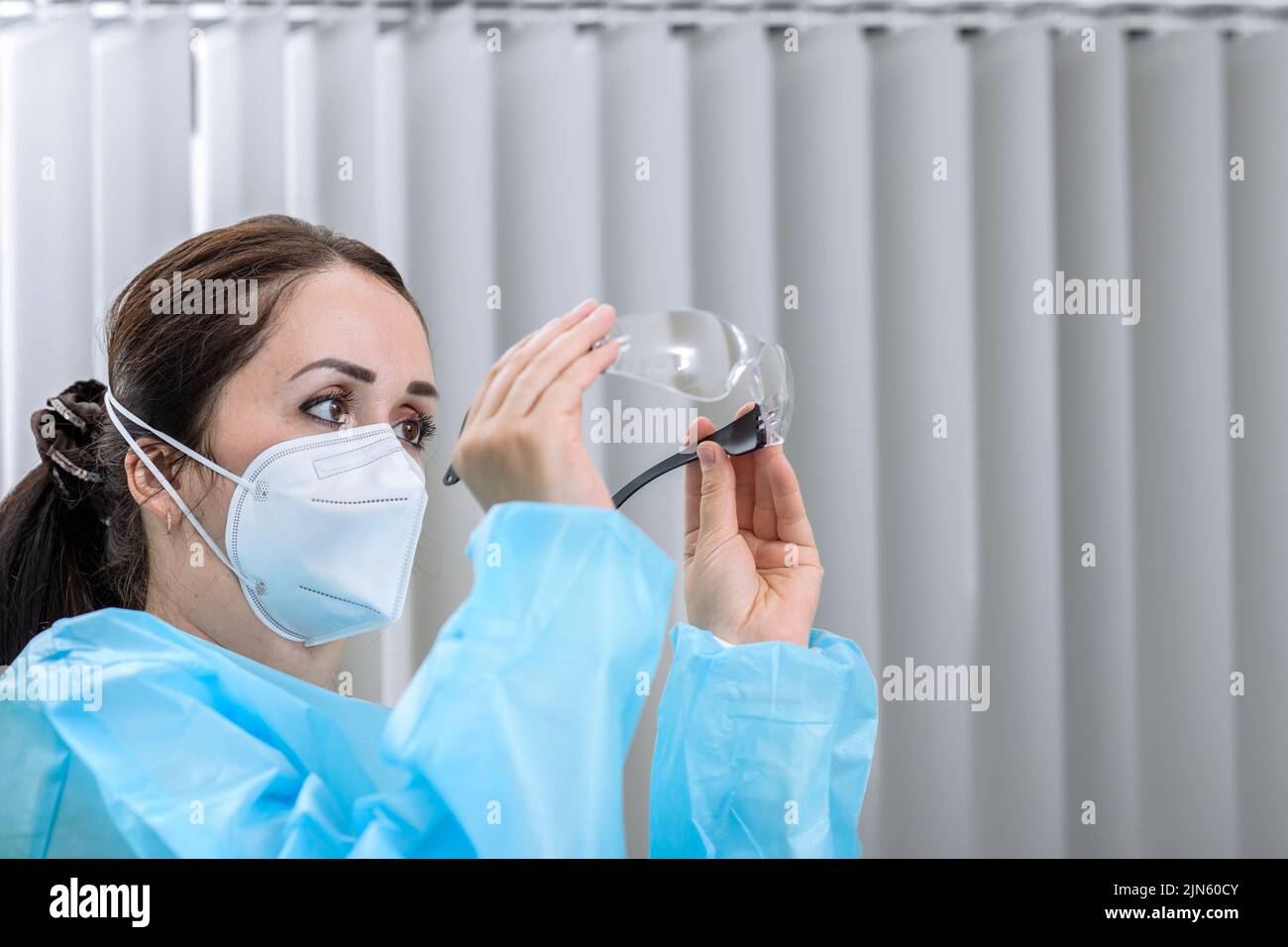 Die Krankenschwester überprüft ihre Schutzbrille, während sie im Aufnahmebüro eine N95-Maske auf ihrem Gesicht trägt Stockfoto