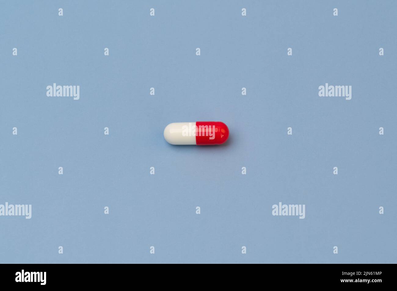 Einzelne rote und weiße Vitamin-Tablette Ergänzung Medikament auf blauem Hintergrund Stockfoto