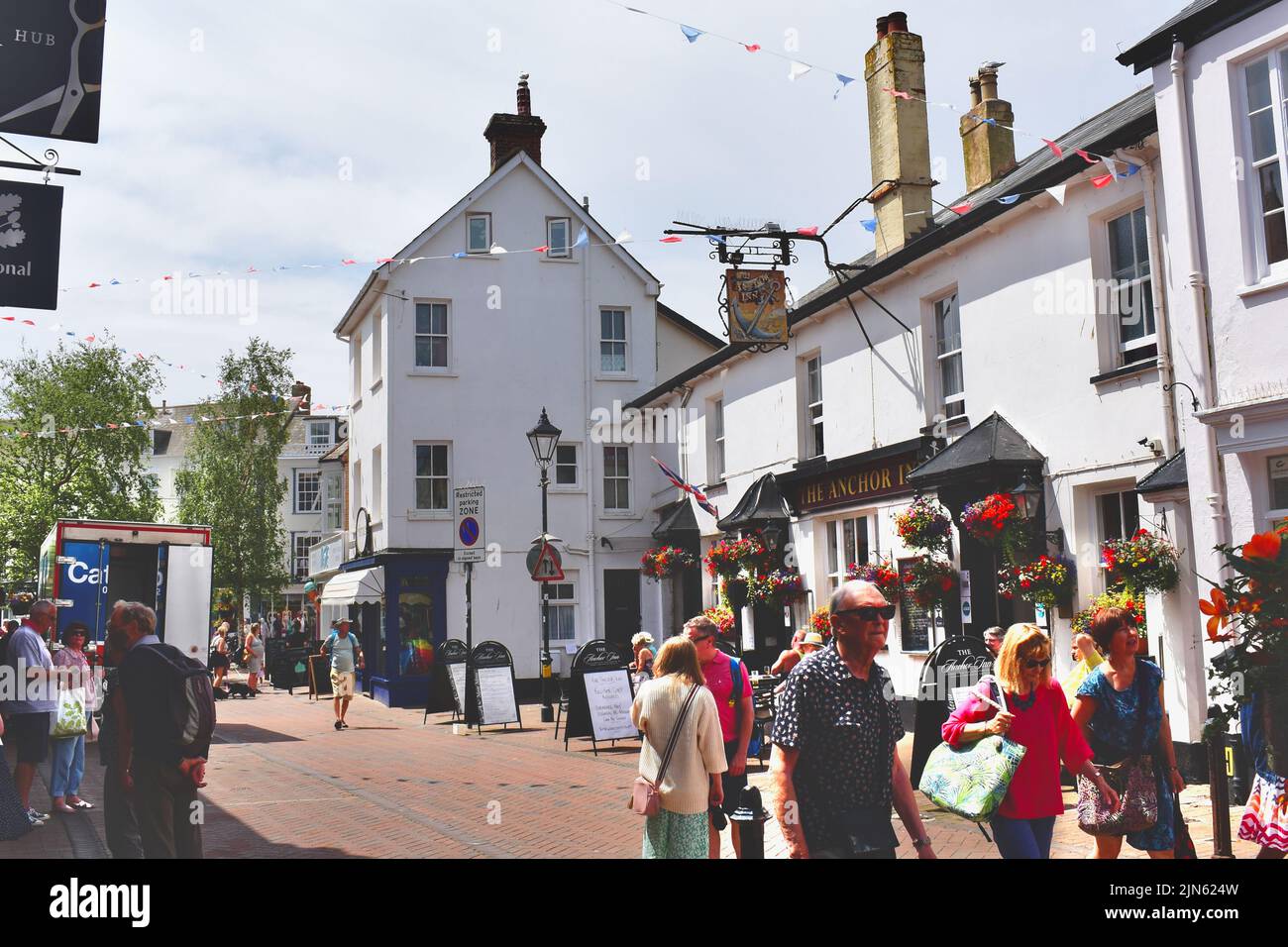 Eine geschäftige Straßenszene mit Urlaubern im Zentrum von Sidmouth. Besucher sitzen vor dem Anchor Inn, beliebt für Mittag- und Abendessen. Stockfoto