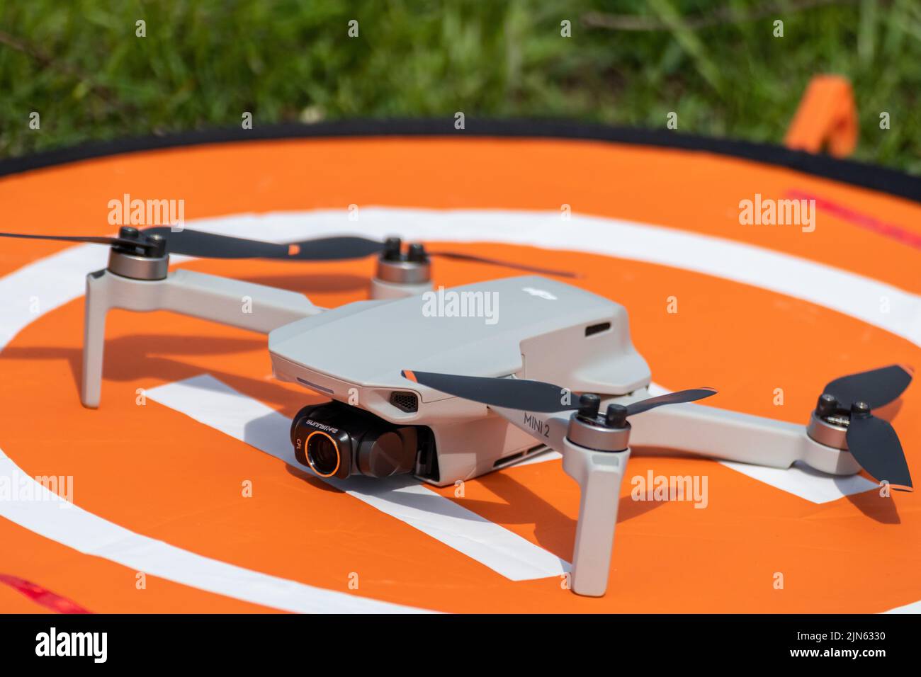 Kharkiv, Ukraine - 22. April 2021: DJI Mavic Mini 2 Drohne mit cpl Filter auf oranger Landeplattform. Quadcopter auf klappbarer Startfläche Seitenansicht mit Stockfoto Kharkiv, Ukraine - 22. April 2021: DJI Mavic Mini 2 Drohne mit cpl Filter auf oranger Landeplattform. Quadcopter auf klappbarer Startfläche Seitenansicht mit Stockfoto