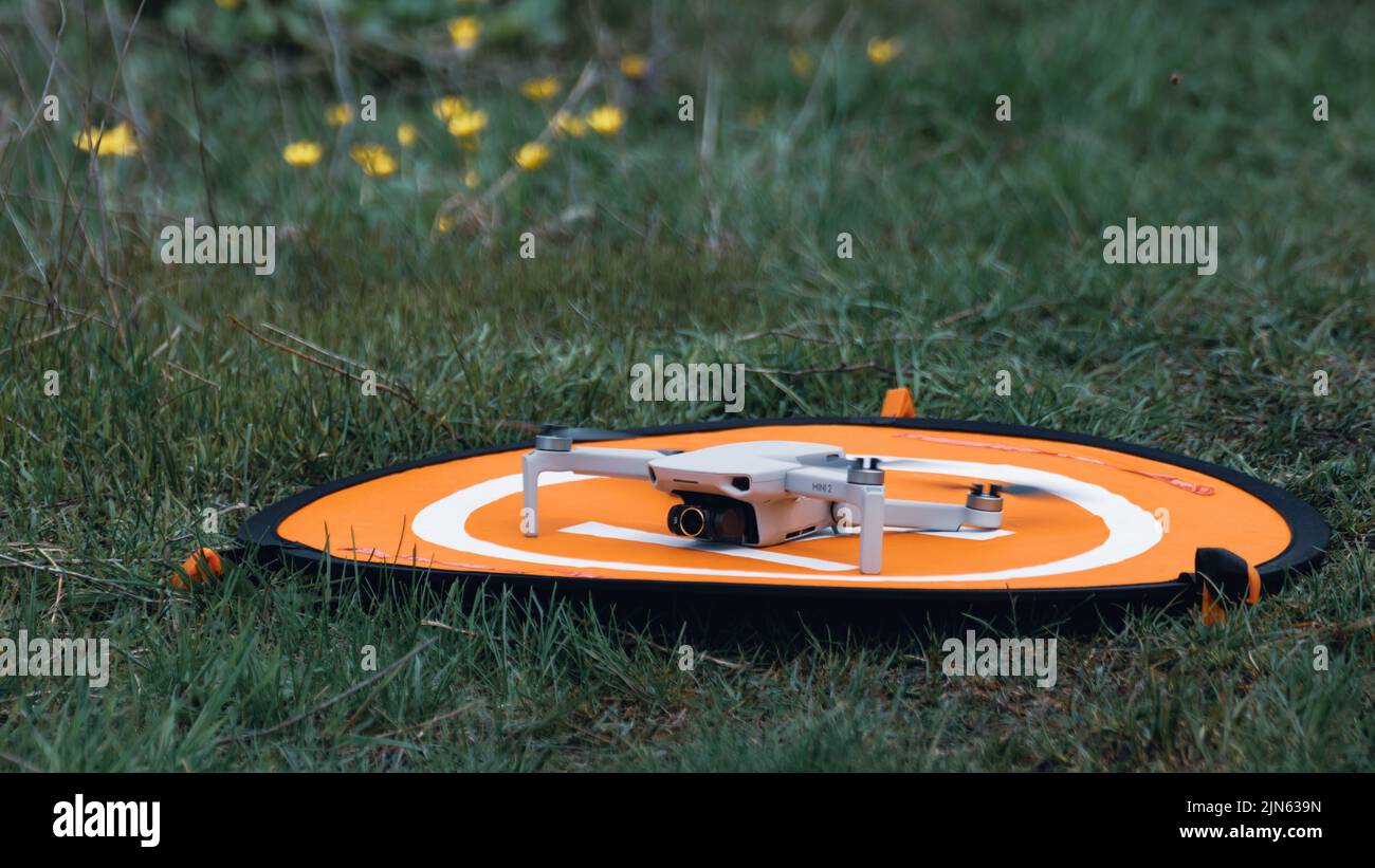 Kharkiv, Ukraine - 22. April 2021: Drohne DJI Mavic Mini 2 auf orangefarbener Landeplattform. Quadcopter auf klappbarer Startmatte auf grünem Rasen mit Hintergrund Stockfoto Kharkiv, Ukraine - 22. April 2021: Drohne DJI Mavic Mini 2 auf orangefarbener Landeplattform. Quadcopter auf klappbarer Startmatte auf grünem Rasen mit Hintergrund Stockfoto