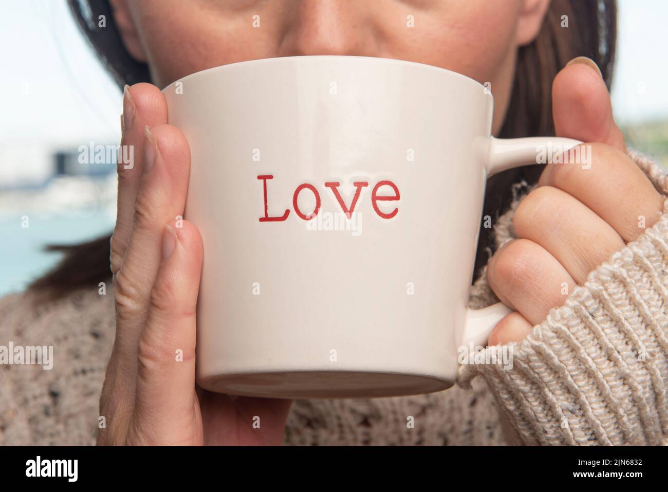Die Frau nippte aus einer Tasse mit der darauf geschriebenen „Liebe“, aus nächster Nähe. Stockfoto
