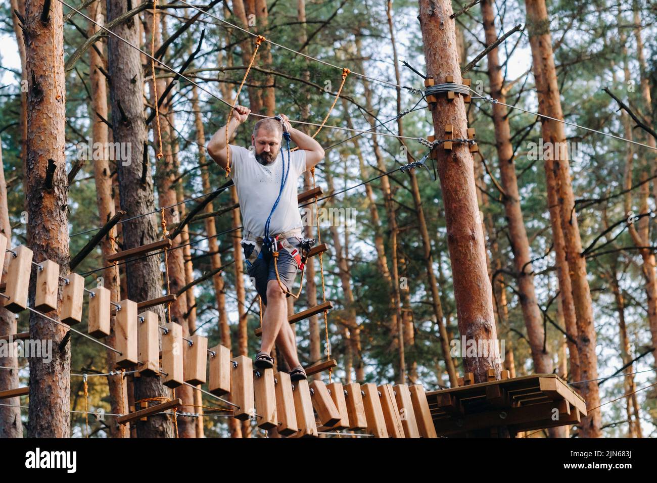 Ein Mann überwindet ein Hindernis in einer Seilstadt. Ein Mann in einem Waldseilpark Stockfoto