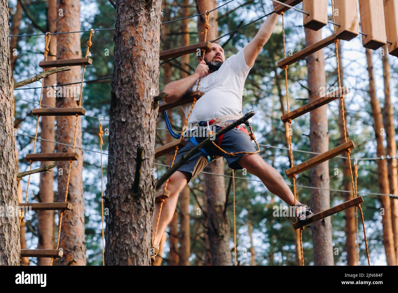 Ein Mann überwindet ein Hindernis in einer Seilstadt. Ein Mann in einem Waldseilpark Stockfoto