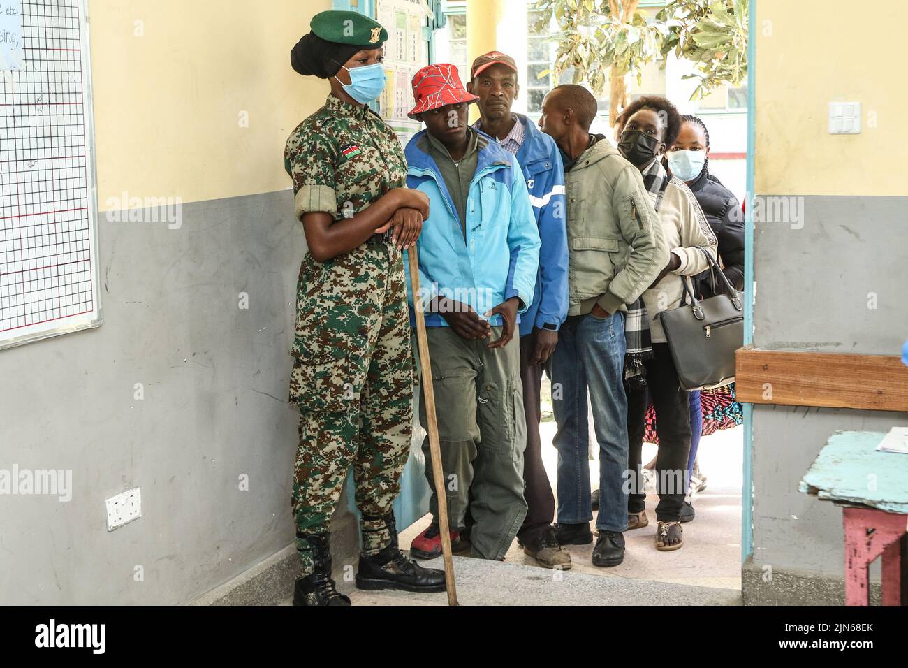 Nakuru, Kenia. 09. August 2022. Ein Beamter des Nationalen Jugenddienstes steht am Eingang eines Wahlbezirks auf Wache, während die Wähler in der Warteschlange der Nakuru Boys High School im Wahlkreis Nakuru Town East warten. Die Kenianer haben am Dienstagmorgen, dem 9. August 2022, mit der Wahl ihres bevorzugten Präsidenten und der Mitglieder der nationalen und der Bezirksversammlungen begonnen. (Foto von James Wakibia/SOPA Images/Sipa USA) Quelle: SIPA USA/Alamy Live News Stockfoto