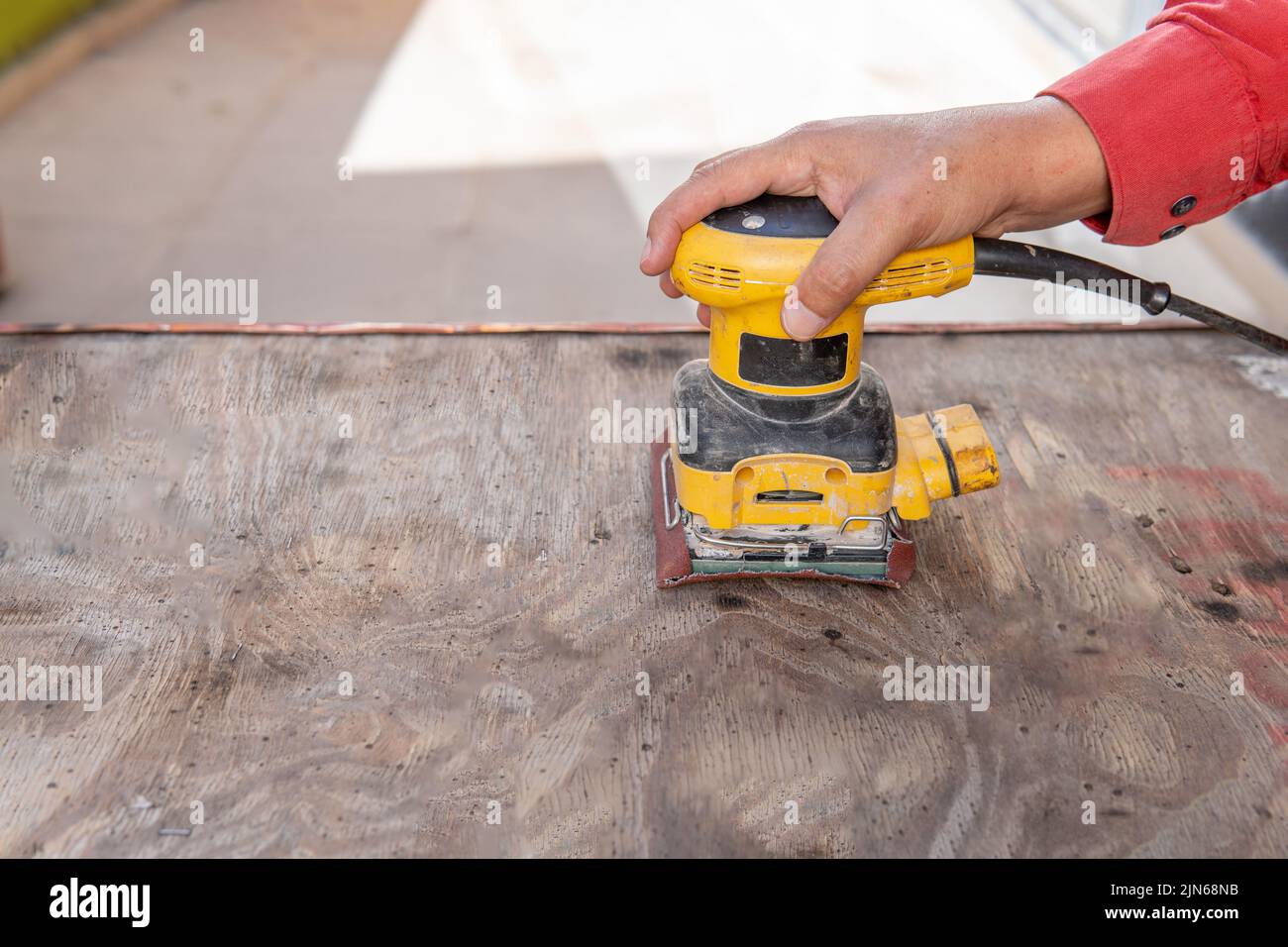 Nahaufnahme der Hand eines Mannes, der ein Stück Holz mit einem elektrischen Schleifer auf einer Terrasse im Freien schleift Stockfoto