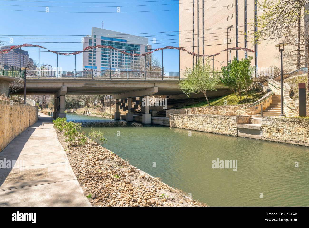 Gehweg neben dem Fluss in der Nähe der Bidge und Gebäude in San Antonio, Texas. Betonweg mit Laternenpfosten und Blick auf eine Treppe rechts n Stockfoto