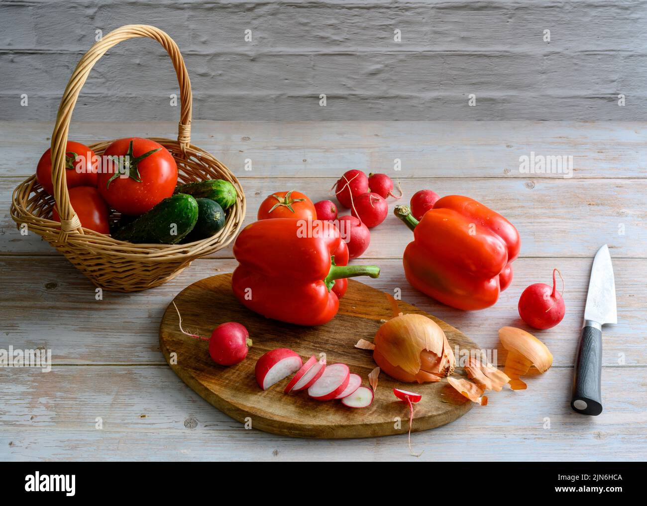 Paprika, Radieschen in Scheiben und Zwiebel neben Tomaten und Gurken auf einem Holztisch Stockfoto