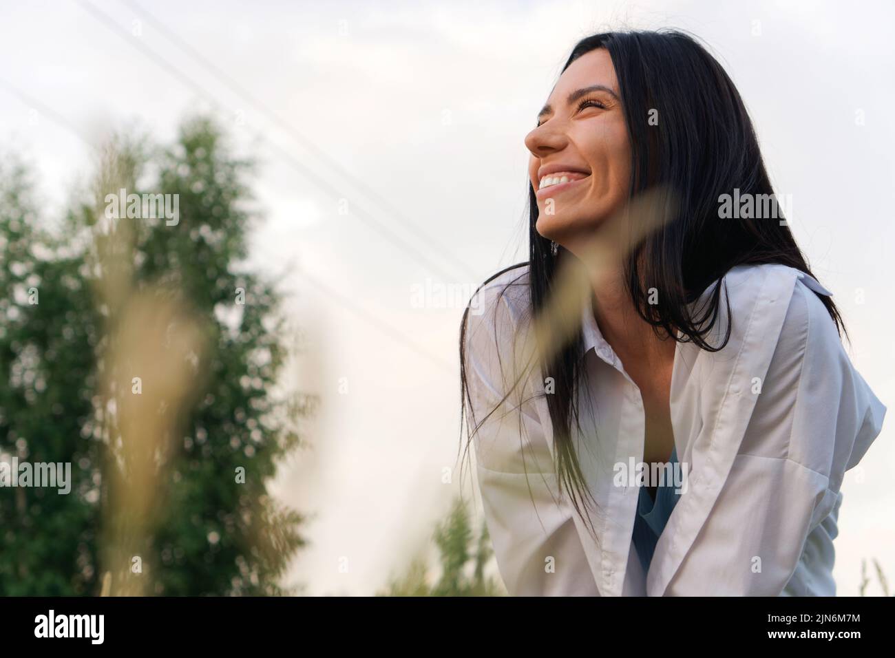 Junge lächelnde Frau im weißen Hemd, die die Natur in der Wiese genießt Stockfoto