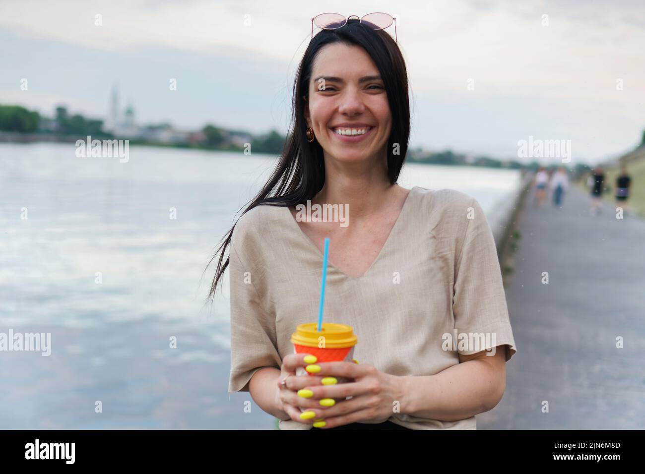 Junge weibliche Brünette lachend hält Kaffee-Tasse auf dem Ufer Stockfoto