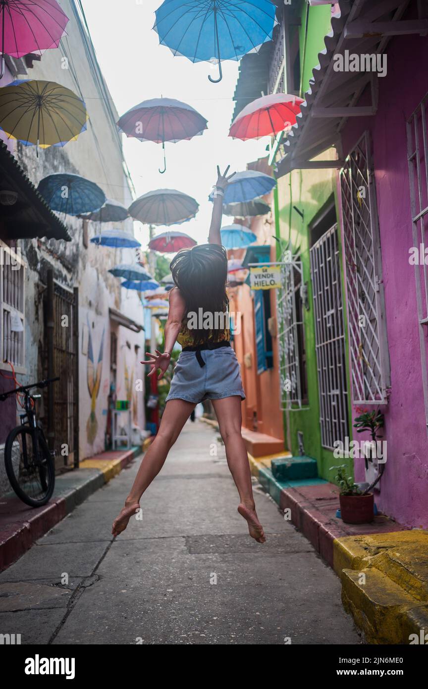 Junge Frau springt in der beliebten Umbrella-überdachten Straße im coolen Viertel Getsemani, Cartagena de Indias, Kolumbien Stockfoto