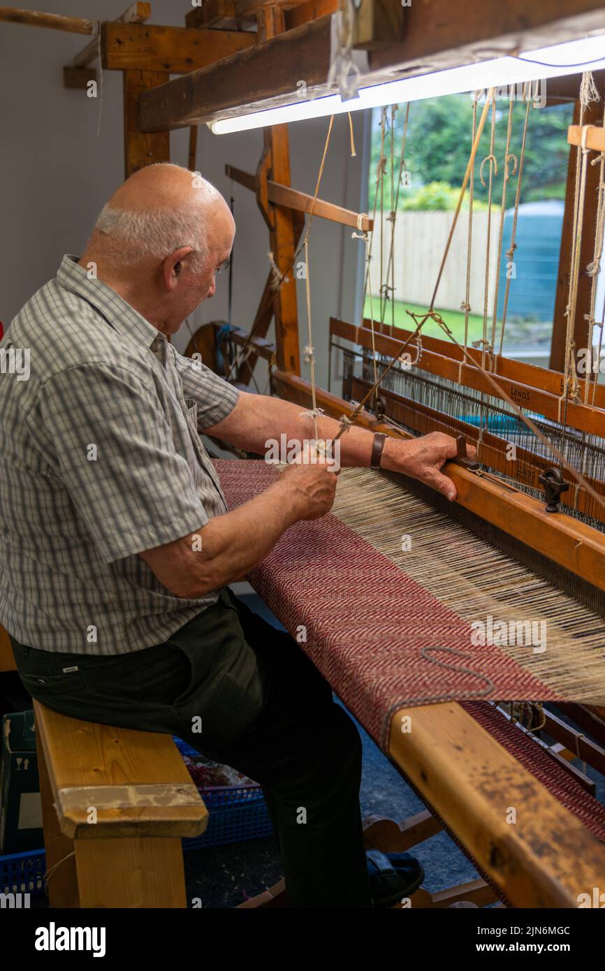 Ardara, Irland - 13. Juli 2022: Meisterin bei der Arbeit an einem traditionellen Holzwebstuhl und der Handweberei von Wollheringbone Stockfoto