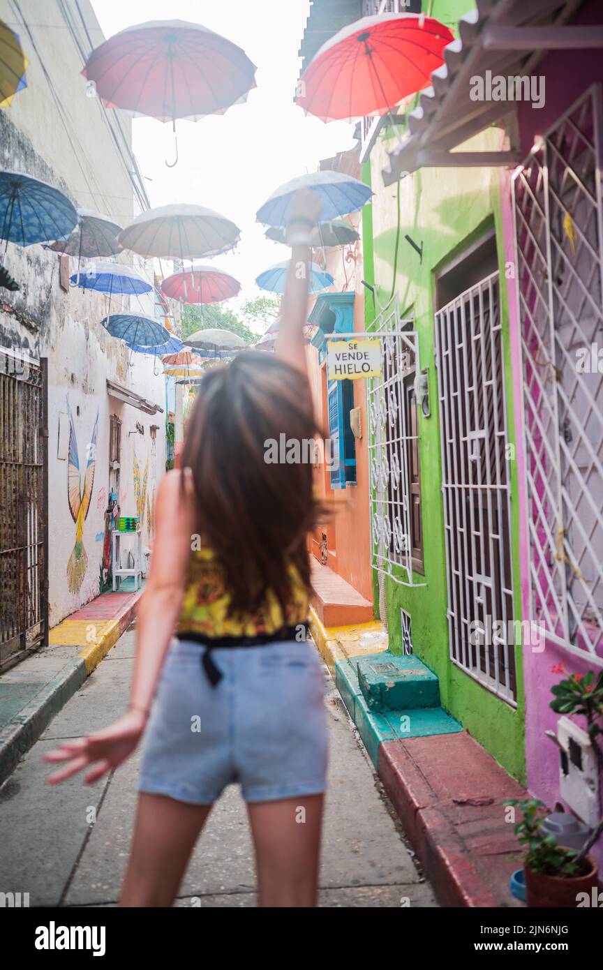 Junge Frau springt in der beliebten Umbrella-überdachten Straße im coolen Viertel Getsemani, Cartagena de Indias, Kolumbien Stockfoto
