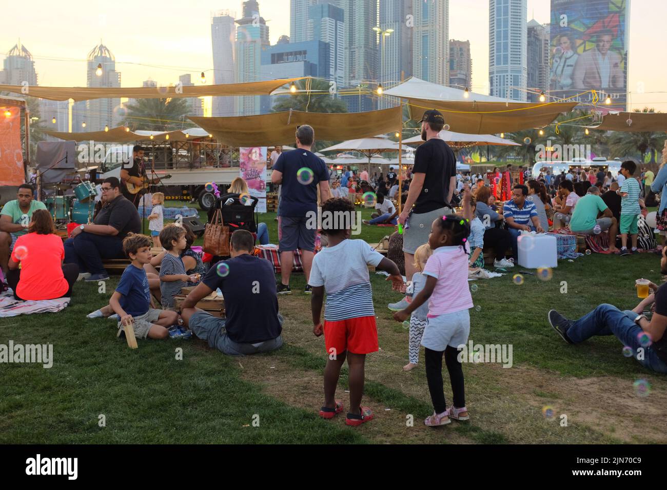 Dubai, Vereinigte Arabische Emirate - 26. März 2016: Beim Food Truck Jam im Emirates Golf Club picknicken verschiedene Menschen auf dem Rasen. Kinder spielen mit Blasen. Stockfoto