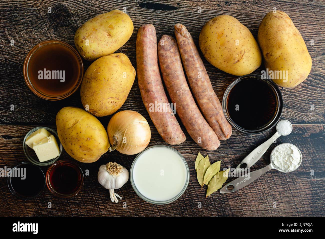 Overhead-Ansicht der Zutaten für Bangers und Maische mit Stout und Zwiebelsoße: Irische Würstchen, Kartoffeln und andere rohe Zutaten auf einem Holzhintergrund Stockfoto