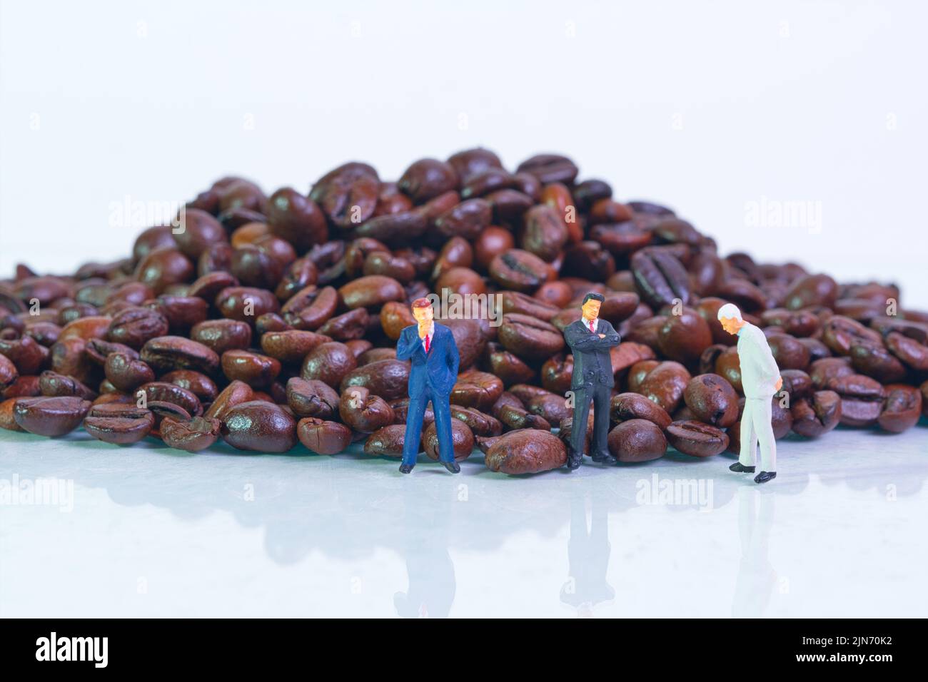 Ein hoher Stapel gerösteter Kaffeebohnen auf weißem Hintergrund, Geschäftsleute stehen vor und verhandeln Stockfoto