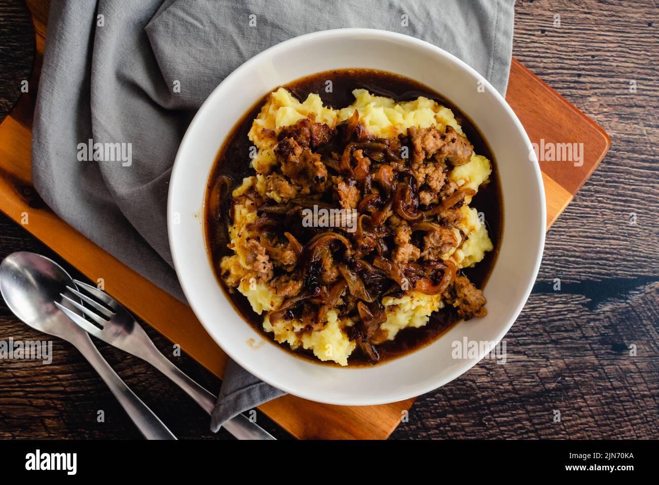 Eine dekonstruierte Version von Bangers and Mash mit Stout und Zwiebelsoße: Kartoffelpüree mit Stücken irischer Wurst, Zwiebeln und Soße Stockfoto