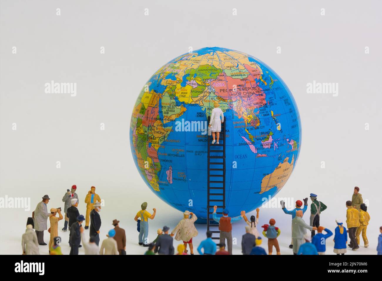 Menschen stehen um einen Globus herum und beobachten, wie sie von einer Wissenschaftlerin auf einer Leiter, Vorderansicht, hellem Hintergrund untersucht wird Stockfoto