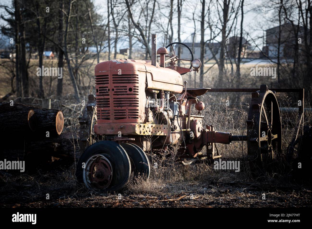 Eine Nahaufnahme eines alten roten Traktors, der auf einem Feld in der Nähe der Farm unter der Sonne geparkt ist Stockfoto