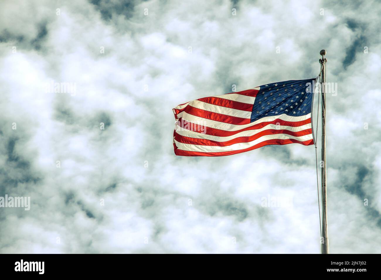 Die Vereinigten Staaten von Amerika rot-weiße und blaue Flagge, die in einer Brise auf einem Fahnenmast vor dramatisch bewölktem Himmel bröcklig knusprig ist - kopieren Sie den Raum Stockfoto
