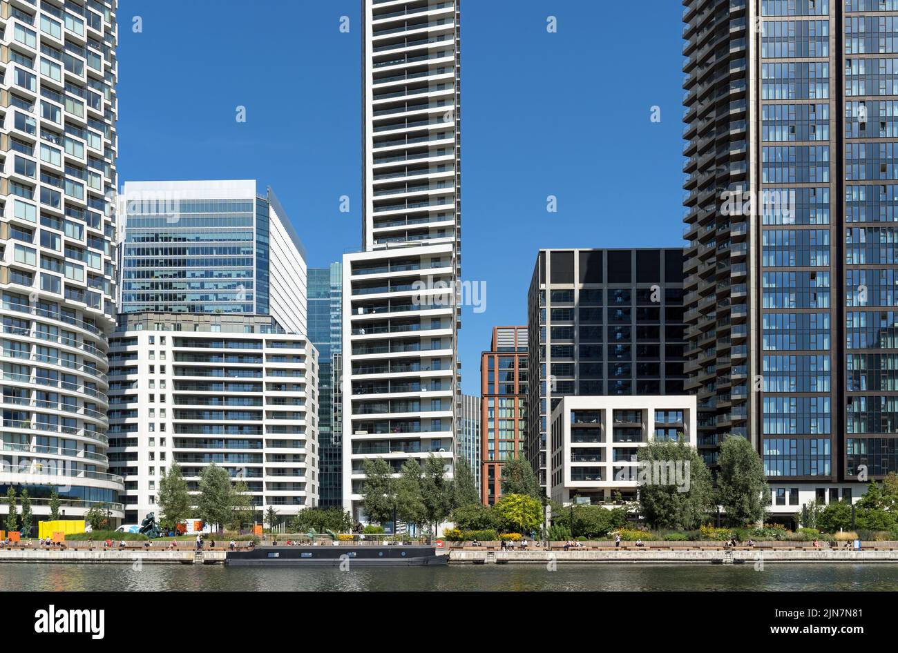 Wood Wharf ein neues Wohnviertel in den Docklands, Hochhäuser in der Sommersonne mit Menschen, die auf der Seite der Docks sitzen. Stockfoto