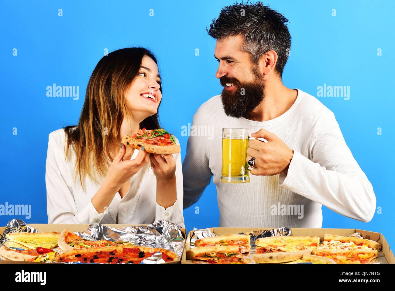 Glückliches Paar, das am Tisch sitzt, Pizza isst und Bier trinkt, hat Spaß zusammen. Lieferung von Lebensmitteln. Stockfoto