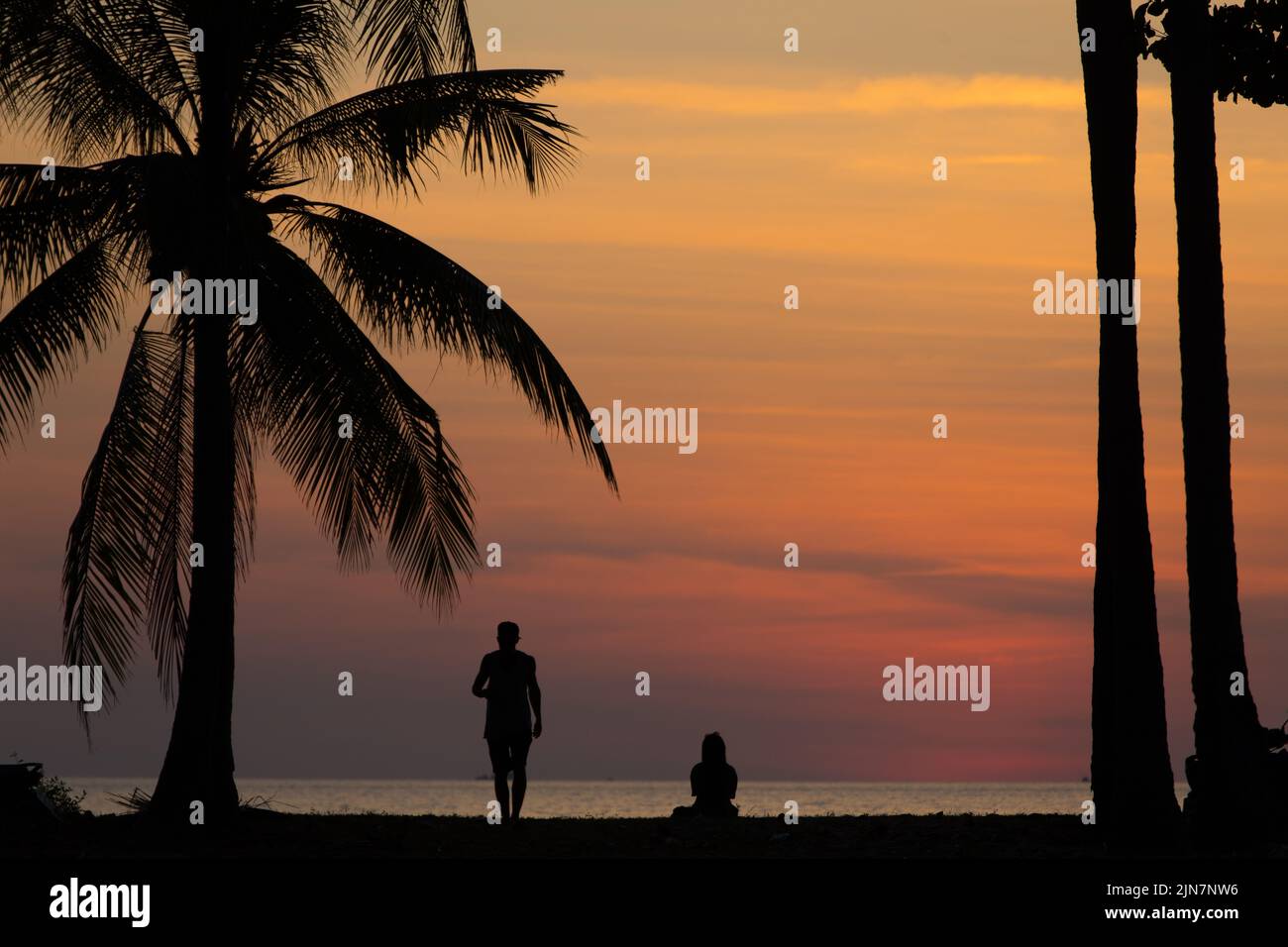 Tropisches Strandpaar bei Sonnenuntergang und Kokospalmen. Ein Paar genießt die wunderschönen Sonnenuntergangsfarben der thailändischen Andamanenküste Stockfoto