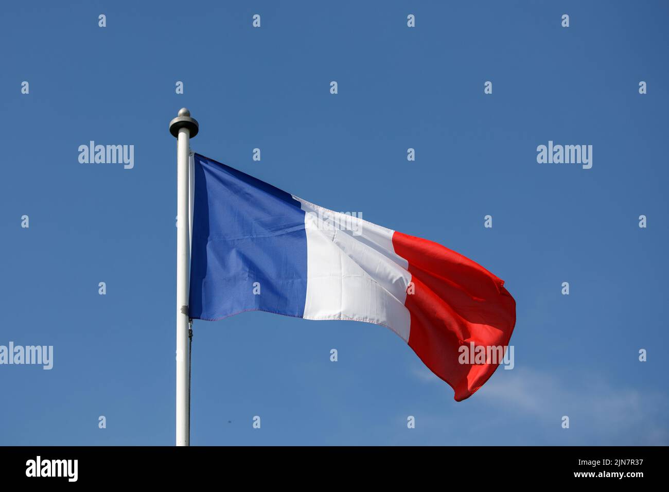 Französische Flagge flattert im Wind mit blauem Himmel Hintergrund. Tricolor auf einem weißen Fahnenmast Stockfoto