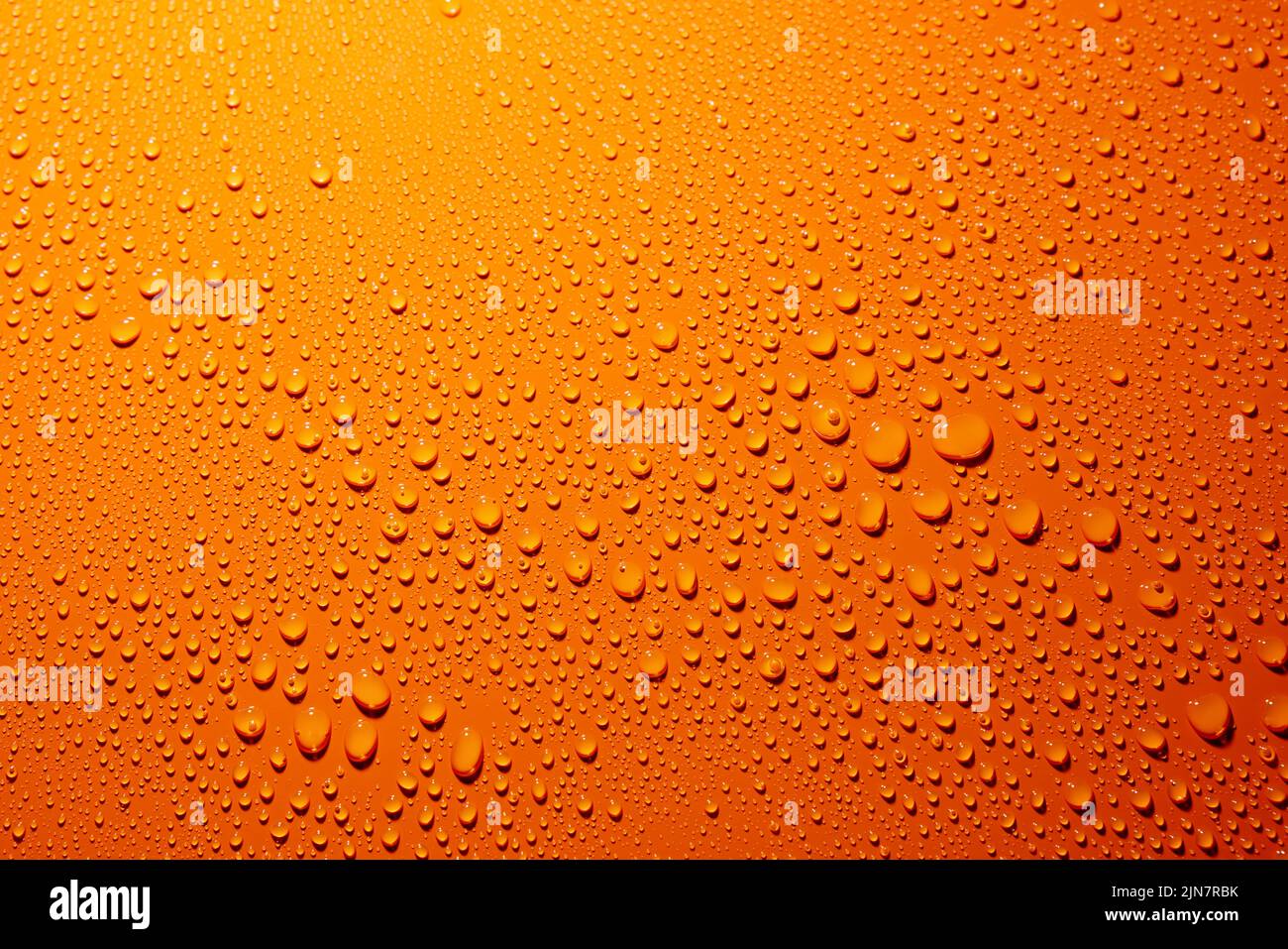 Eine Nahaufnahme von Wassertropfen auf einer orangefarbenen Oberfläche Stockfoto