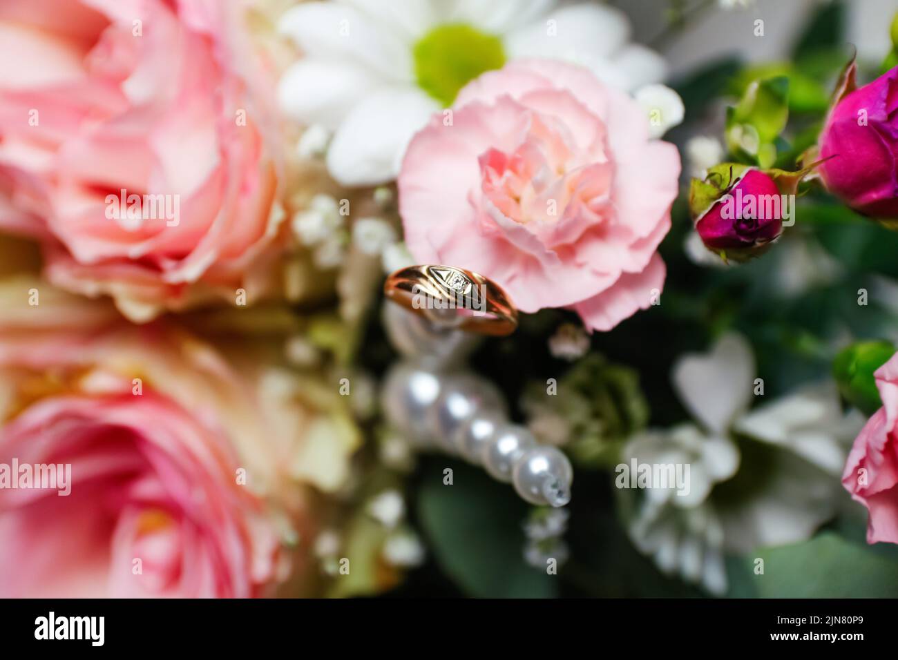 Unschärfe-Effekte auf einen goldenen Ehering. Rosa Blumen und zwei goldene Eheringe auf weißem Hintergrund. Eheringe auf der Rose. Nicht fokussiert. Stockfoto