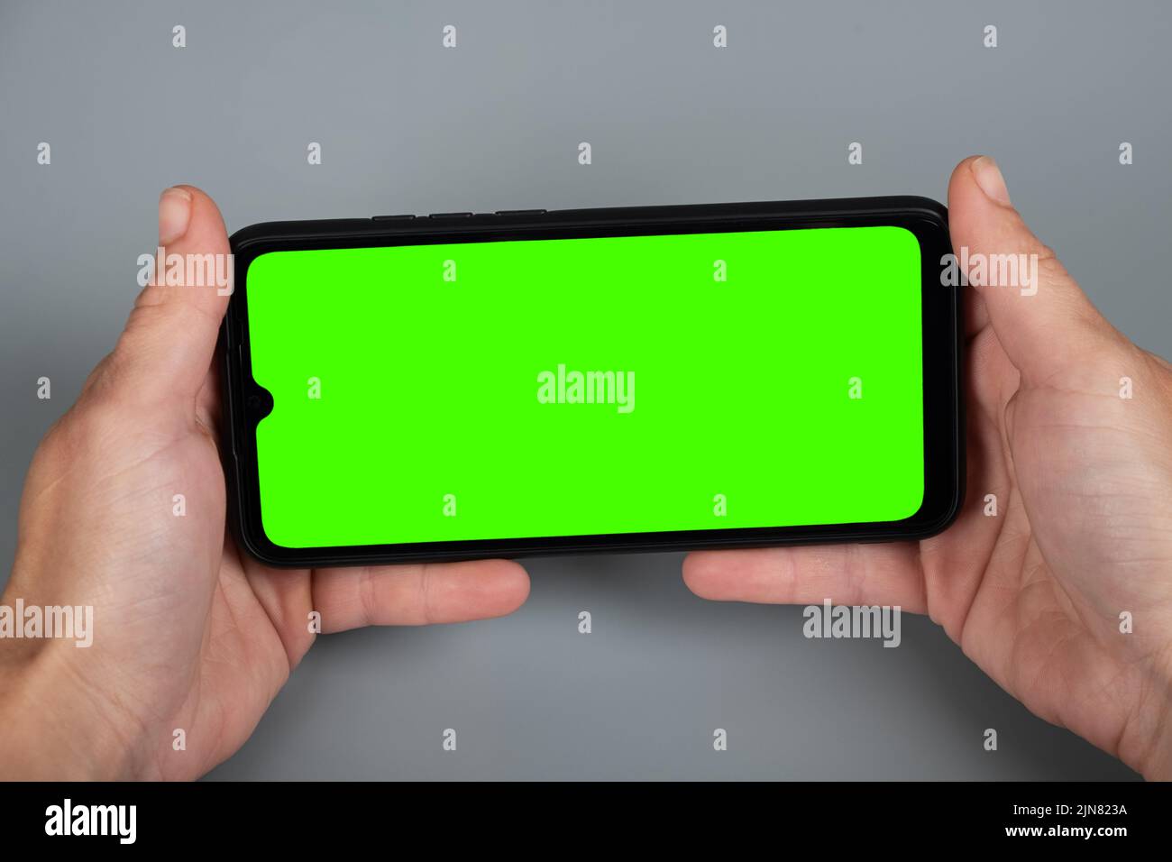 Hände halten das Telefon horizontal, grüne Chroma-Taste Mockup auf dem Smartphone. Stockfoto