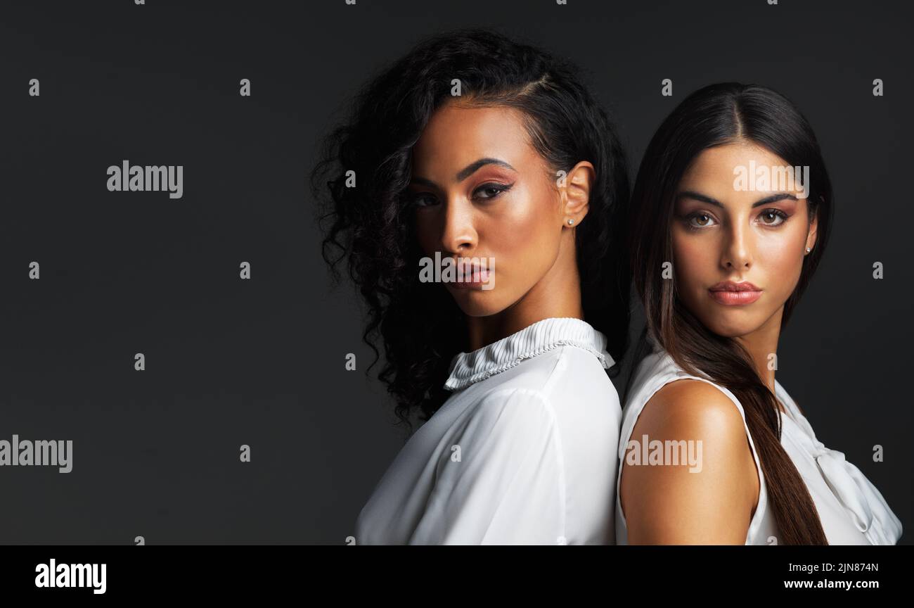 Alles an ihnen ist atemberaubend. Porträt zweier attraktiver junger Frauen, die sich vor dunklem Hintergrund in einem Studio Rücken an Rücken posieren. Stockfoto
