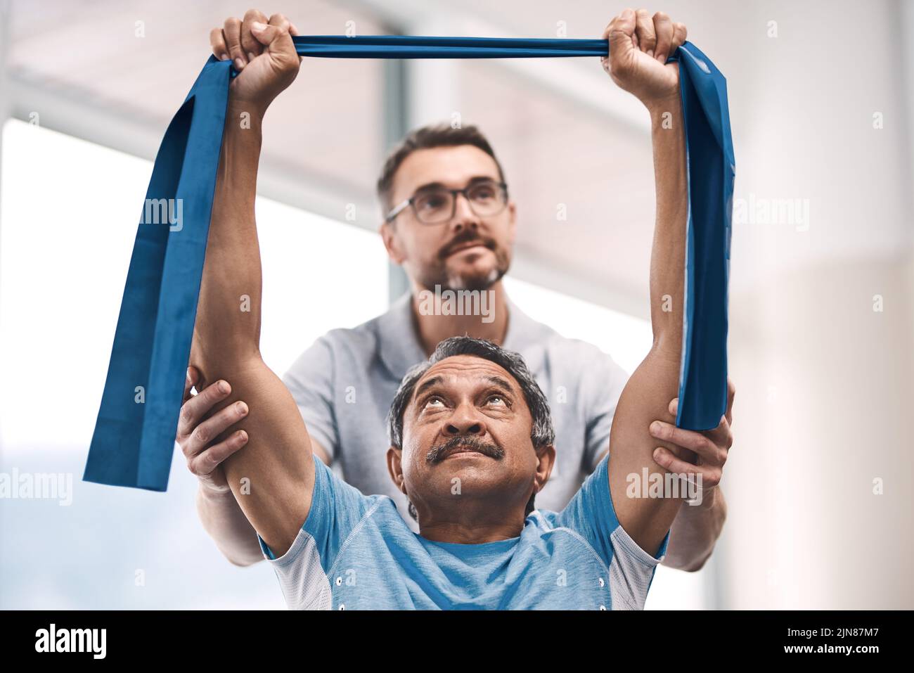 Ein älterer Mann trainiere mit einem Widerstandsband während einer Rehabilitationssitzung mit seinem Physiotherapeuten. Stockfoto