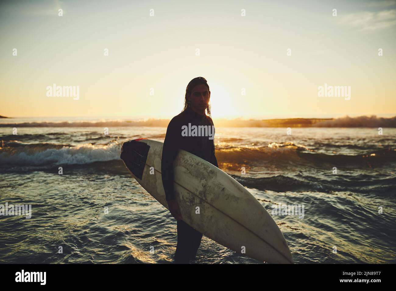 Surfzeit ist meine Zeit. Porträt eines jungen Mannes, der ein Surfbrett am Strand trägt. Stockfoto