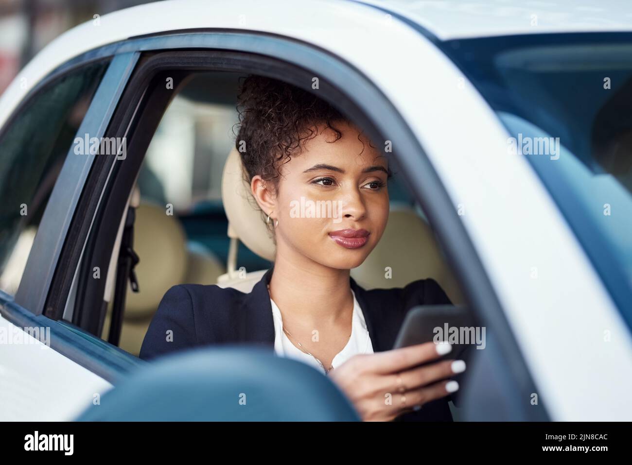 Eine attraktive junge Geschäftsfrau, die ein Smartphone benutzt, während sie in ihrem Auto sitzt. Stockfoto