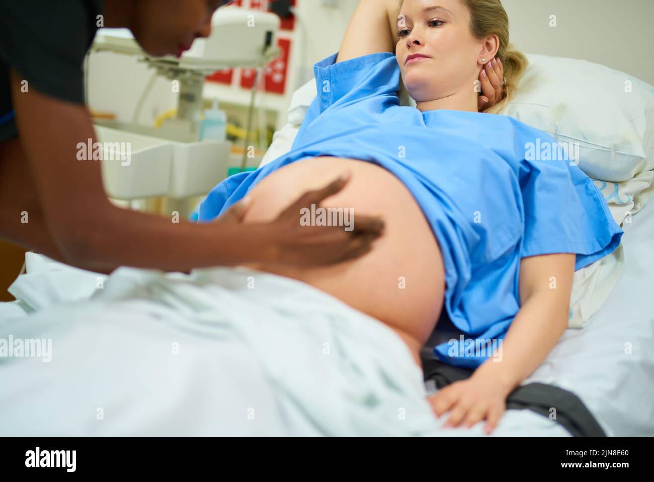 Du und das Baby machen es bisher großartig. Eine junge Schwangere wird von einem Arzt untersucht, während sie in ihrem Krankenhausbett liegt. Stockfoto