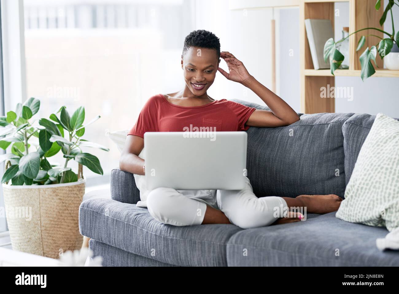 Eine junge Frau, die sich zu Hause auf dem Sofa entspannt und einen Laptop benutzt. Stockfoto