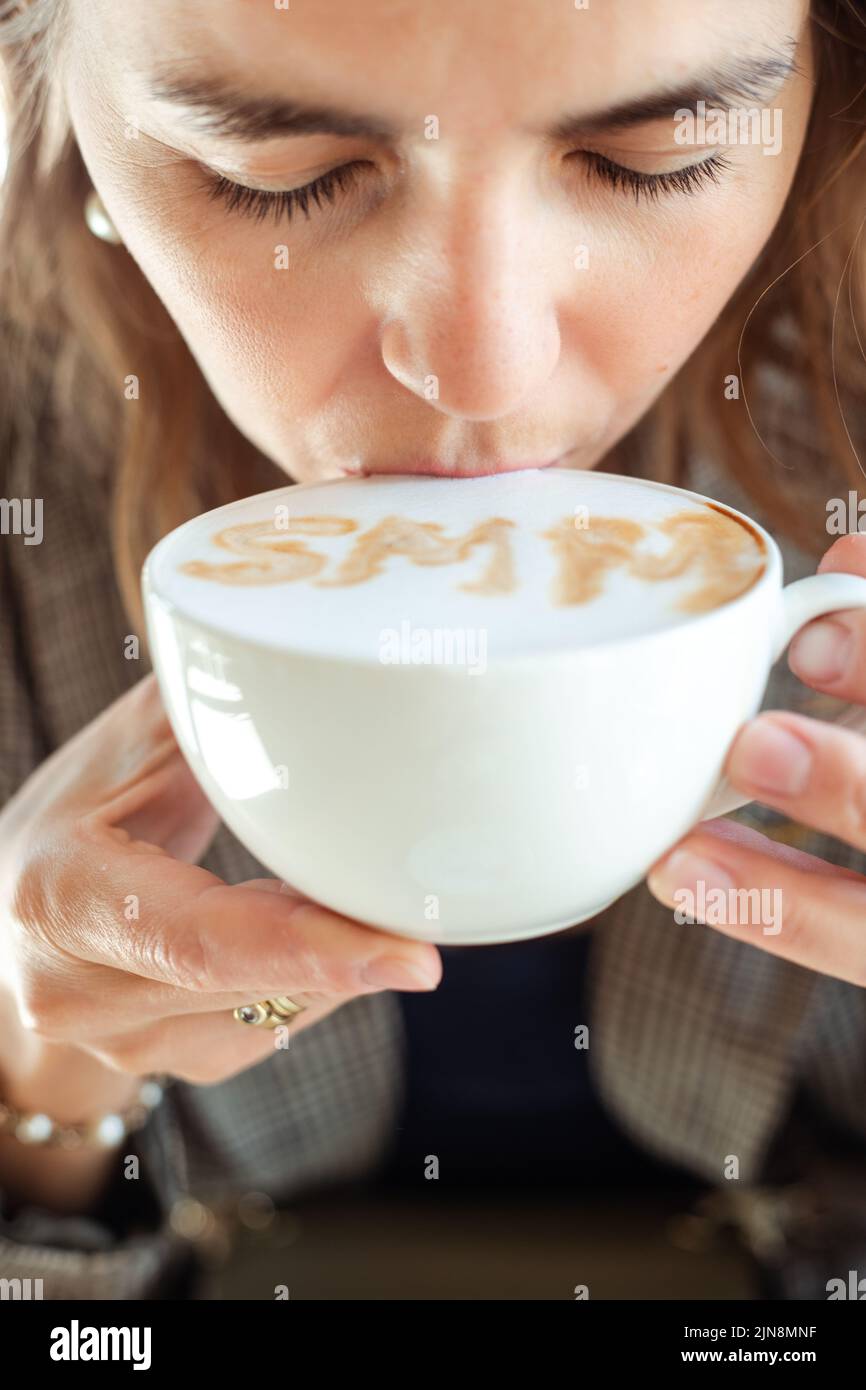 Junge Geschäftsfrau trinkt Kaffee mit heißem Geschmack und weißem Schaum mit Vergnügen und geschlossenen Augen aus der Nähe. Social Media Marketing, SMM, Promotion Stockfoto