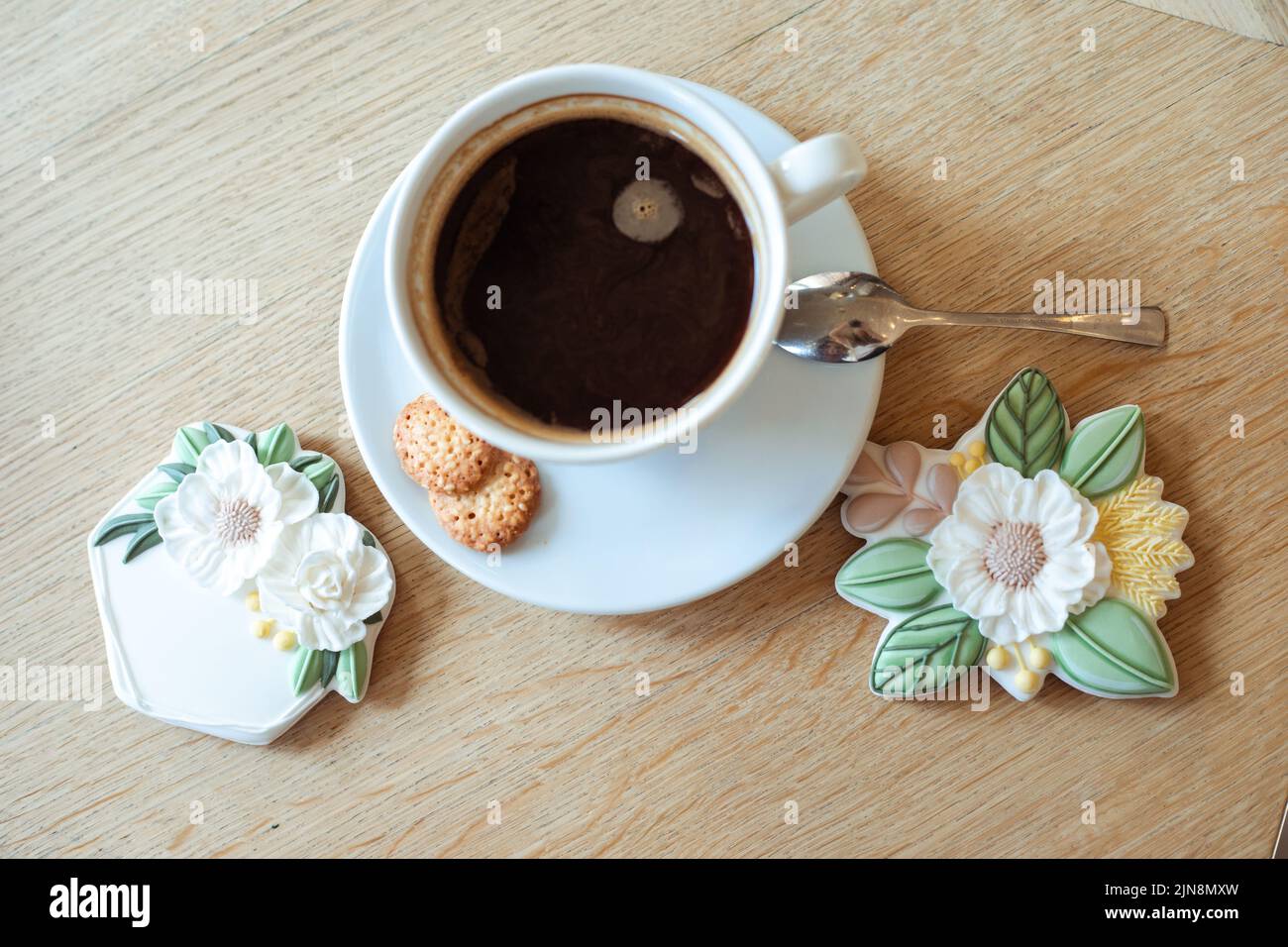 Tasse heißen aromatisierten schwarzen Kaffee mit weichem Schaum auf der Untertasse und schöne Puderblume geformten Cookies auf dem Tisch Draufsicht Nahaufnahme, freie Kopie Platz. Catering Stockfoto