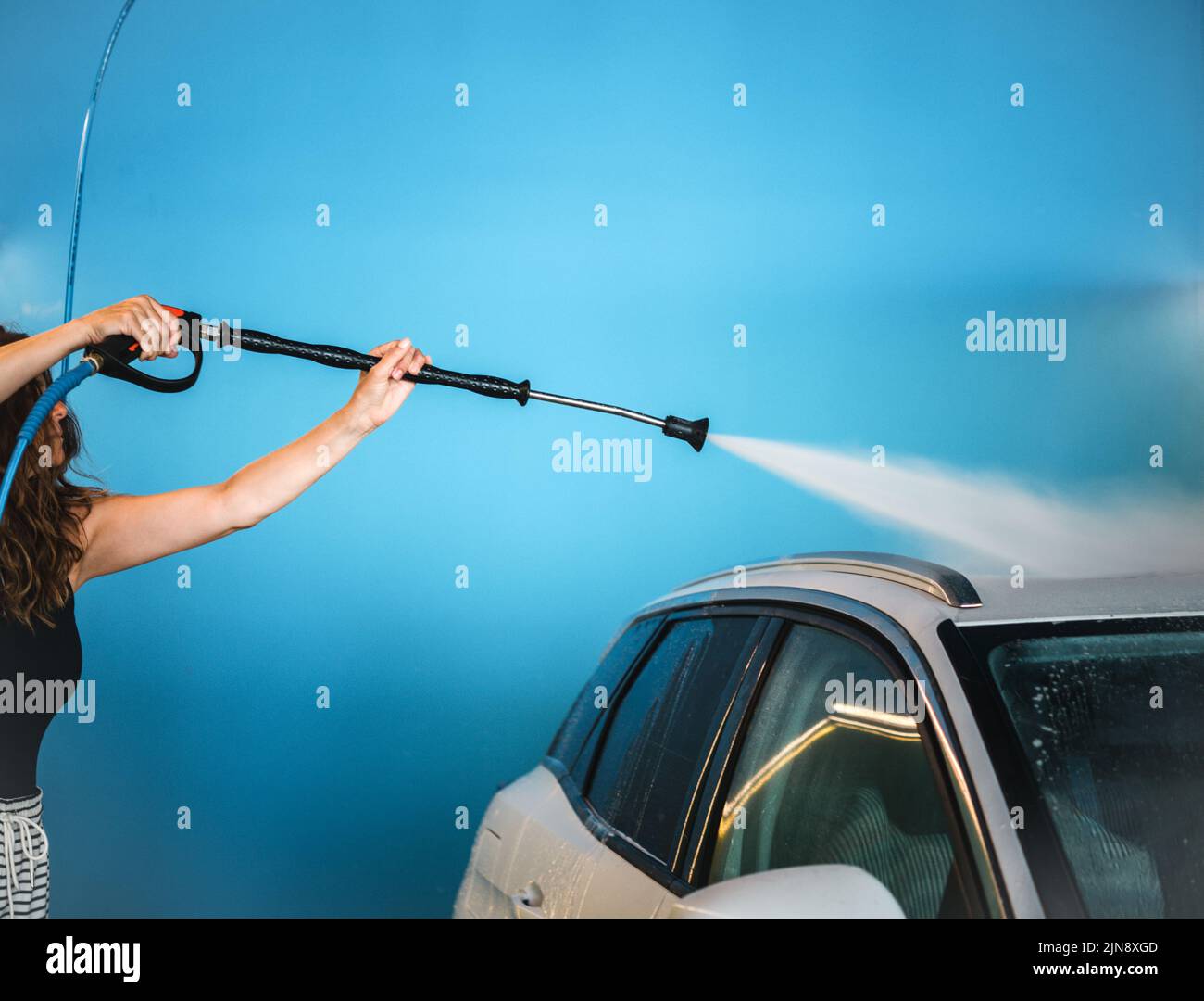 Frau, die Auto vor blauem Hintergrund waschen Stockfoto