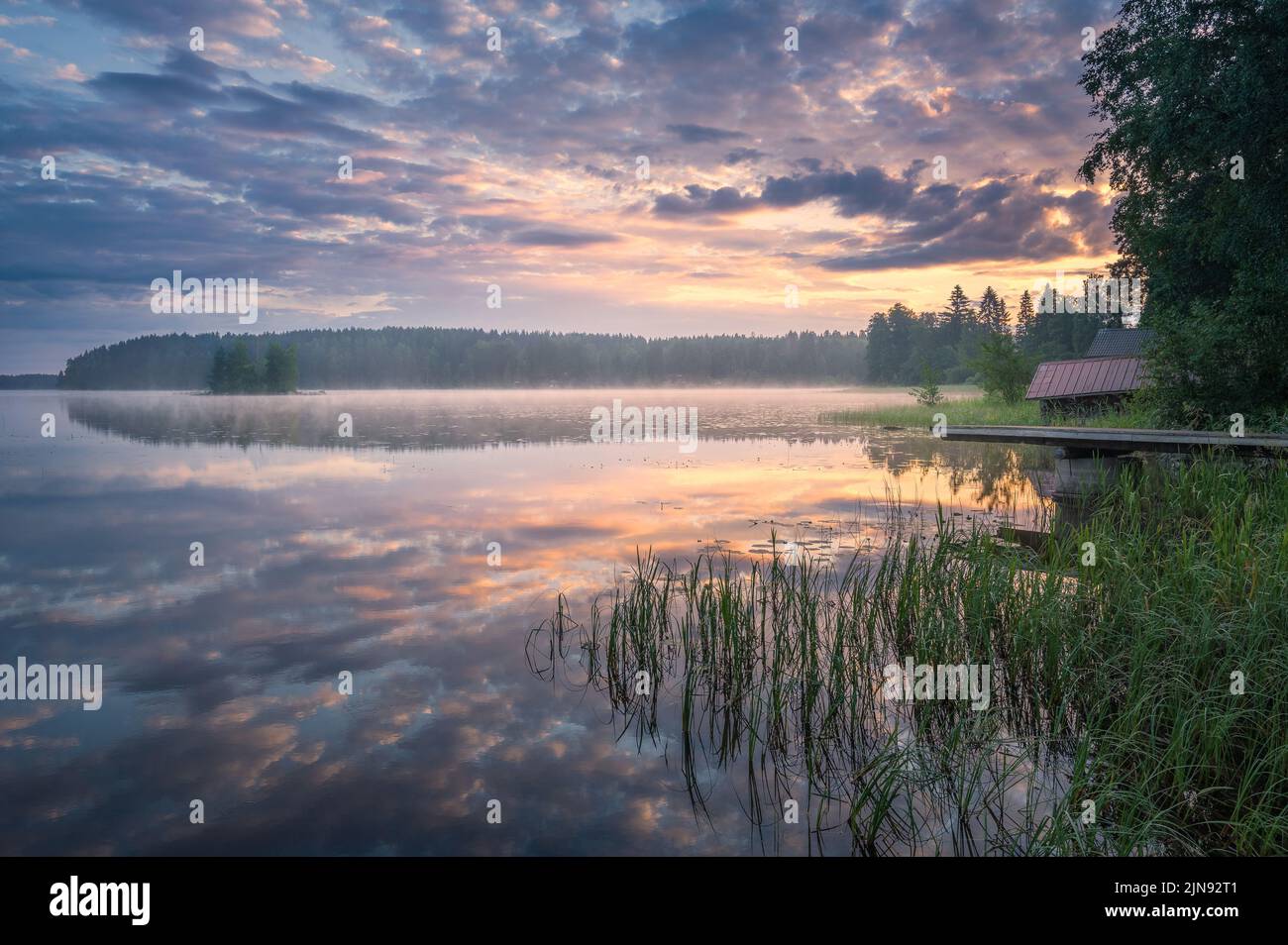 Schöner Sonnenaufgang in einem ruhigen See am Sommerabend in Finnland mit Pier Stockfoto
