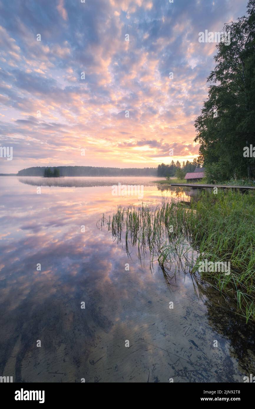 Schöner Sonnenaufgang in einem ruhigen See am Sommerabend in Finnland mit Pier Stockfoto